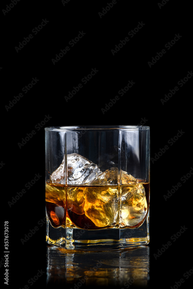 Glass of whiskey with cube ice on black background