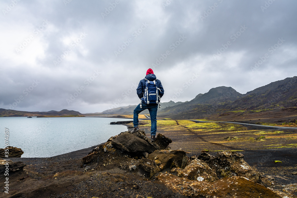 Obraz premium Man hiking in Iceland standing on the peak of rocks with backpack looking at the stunning view near the Kleifarvatn lake in Reykjanesfólkvangur nature reserve park
