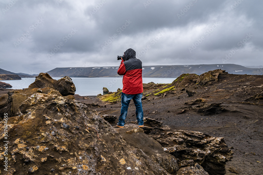 Photographer man taking pictures in Iceland standing on atop of a mountain looking at the stunning view near the Kleifarvatn lake in Reykjanesfólkvangur nature reserve park