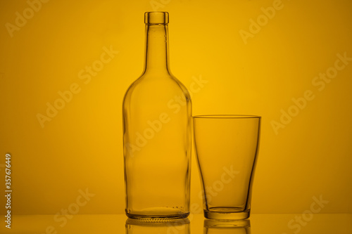 Photo of a bottle and glass with back lighting on a yellow background. empty glass and bottle