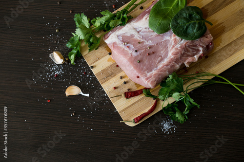 greens, seasonings and meat on a cutting board. a piece of pork, pepper, garlic, salt. Cook at home. fresh food