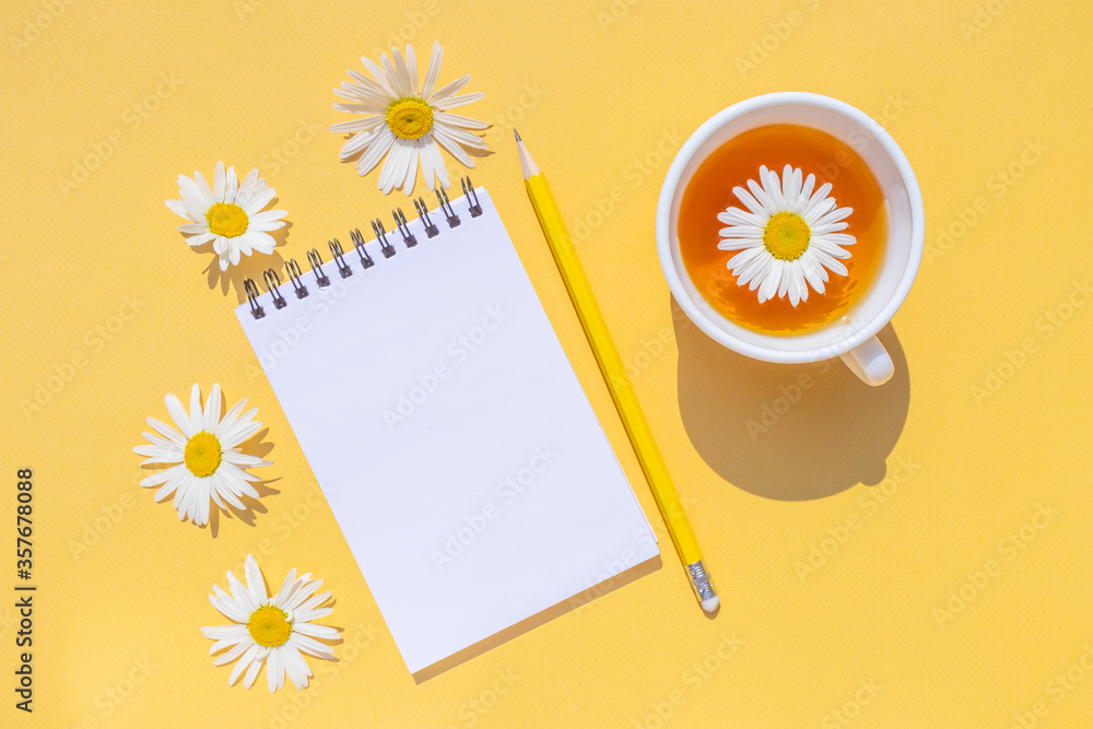 Fototapeta Notebook on a spiral with an empty sheet, a yellow pencil and daisy flowers on a bright yellow background. Copyspace, minimalism, top view. Summer cute funny flat lay.