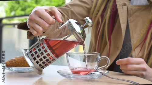 Close up of female hands with cup of fruit tea. Girl with long dreadlocks is drinking in a street coffee shop