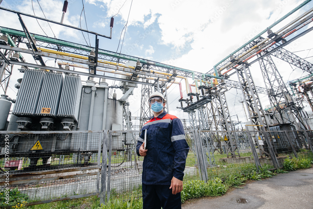 An electrical substation engineer inspects modern high-voltage equipment in a mask at the time of pondemia. Energy. Industry