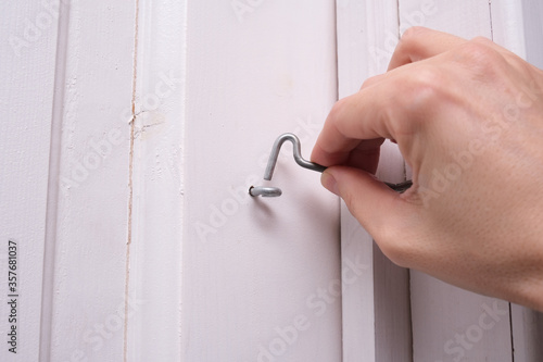 A hand locking a door hook on white wooden door, simple device for home house safety and protection