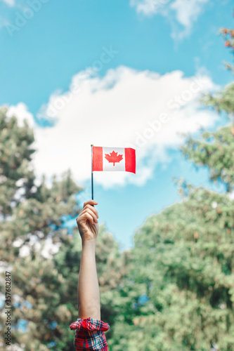 Closeup of woman human hand arm waving Canadian flag against blue sky. Proud citizen man celebrating national Canada Day on 1st of July outdoors.