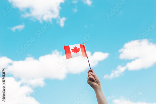 Closeup of woman human hand arm waving Canadian flag against blue sky. Proud citizen man celebrating national Canada Day on 1st of July outdoors.