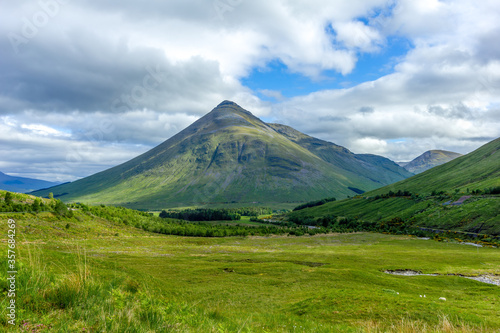 A scenic view of a grassy pyramidal Highland Scottish mountain (Beinn Dòbhrain) with grassy slope under a majestic blue sky and some white clouds