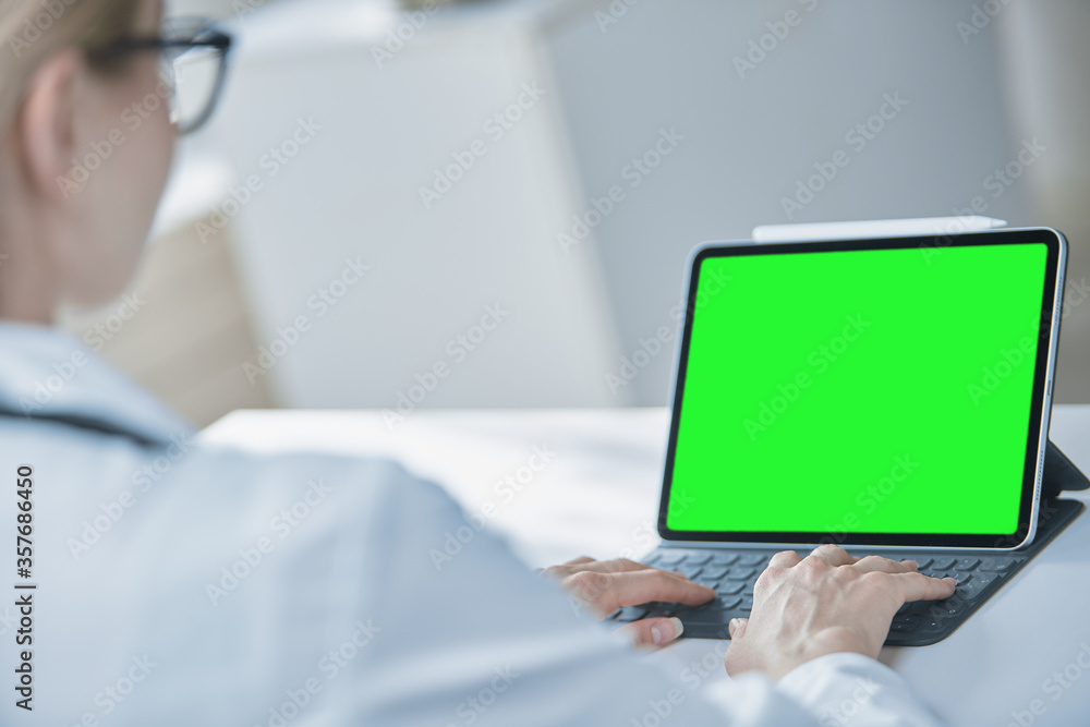 Medical worker a woman in a white coat uses a tablet in the office at the Desk, chromakey on the tablet screen, a view over her shoulder Medical worker a woman in a white coat uses a tablet in the office at the Desk, chromakey on the tablet screen, a view over her shoulder