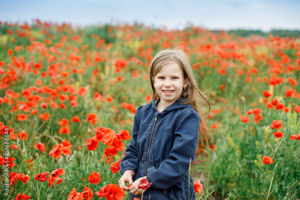 a girl of European appearance in blue clothes stands on a beautiful poppy field against the background of the sunset sky a girl of European appearance in blue clothes stands on a beautiful poppy field against the background of the sunset sky