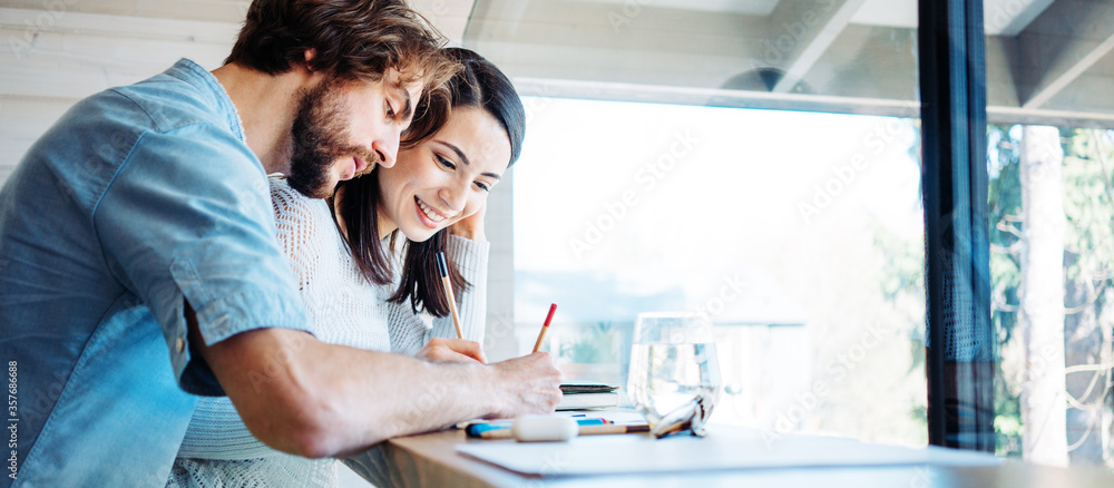 Couple working together at home in bright wooden room in their own house. Remote workplace. Solving tasks at the desk. Wide screen panoramic Couple working together at home in bright wooden room in their own house. Remote workplace. Solving tasks at the desk. Wide screen panoramic