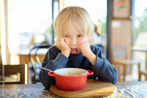 Little child sitting the table in cafe or restaurant and doesn't want to eat. Healthy food. Kids diet. Poor appetite. photo