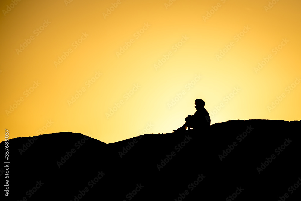 Silhouette of people sitting on large rock near Tofino, British Columbia, at sunset.