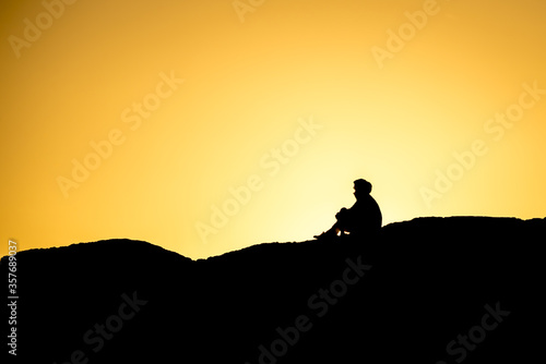 Silhouette of people sitting on large rock near Tofino, British Columbia, at sunset. © chase clausen
