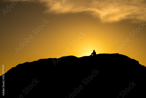 Silhouette of people sitting on large rock near Tofino, British Columbia, at sunset.