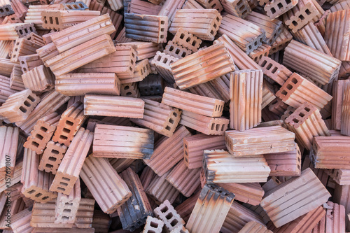 A lot of red bricks are stacked on the floor. Piles of red construction bricks scattered on the ground.