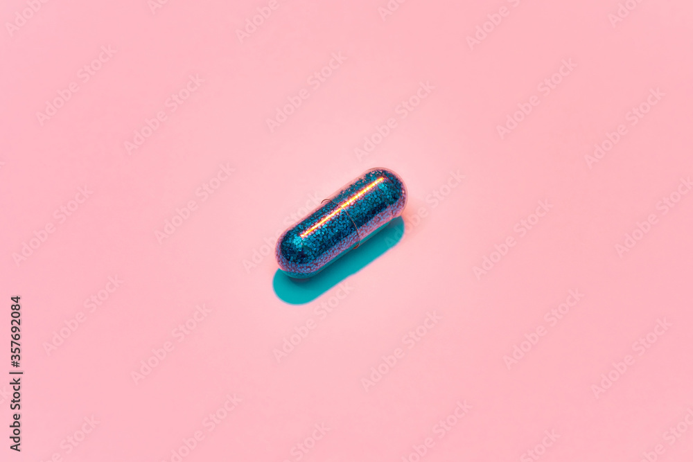 Creative concept with blue glitter pill isolated on pastel pink background. Minimal style, art concept - obrazy, fototapety, plakaty 