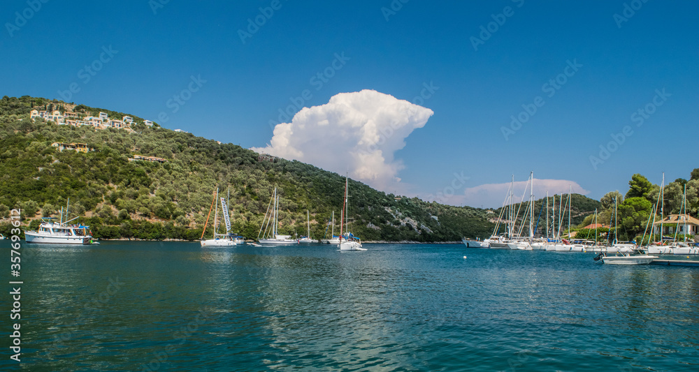 Large cloud formation behind a mountain over a lake with anchored sailing boat at Lefkada island, Greece