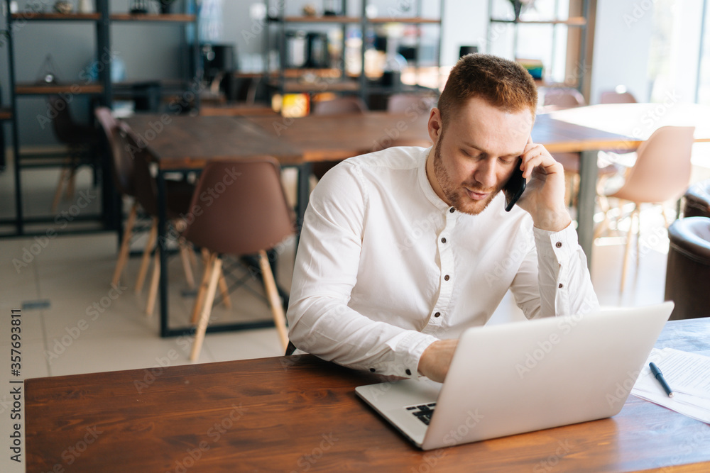 Top view of young business man wearing fashion casual clothing working on laptop and talking on phone, at the table. Concept of office working.