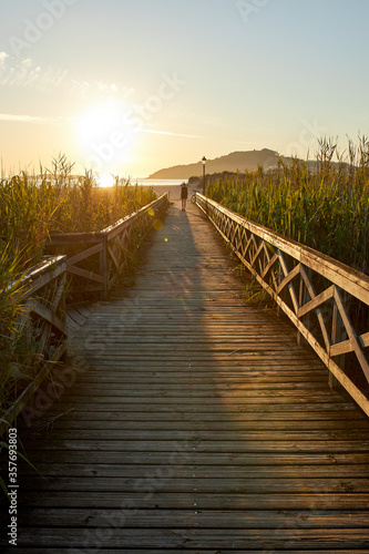 Man walking towards the beach on a wooden path at sunset.