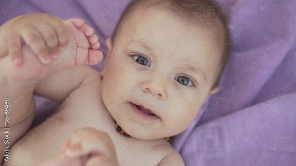 The cute baby boy with brown eyes is lying on his back, touches his legs and smiling. Purple towel on the background The cute baby boy with brown eyes is lying on his back, touches his legs and smiling. Purple towel on the background