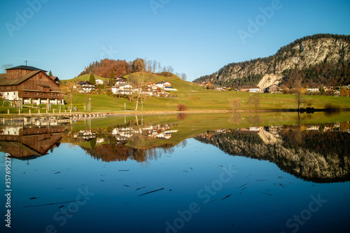 Autumn countryside landscape with reflection of houses in blue lake.