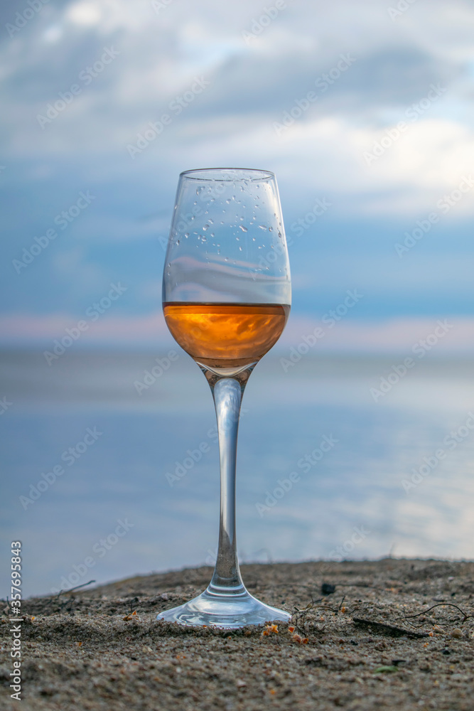 Romantic glass with wine on a background of water and blue sky. With drops on glass and reflection in wine.