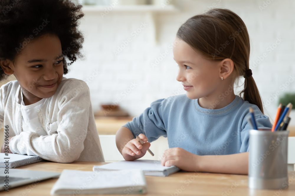 Multi-ethnic funny cheery girls sit at table learning school subject together. Multiracial family daughters do common task, drawing enjoy pastime hobby at home. Self-education, homeschooling concept Multi-ethnic funny cheery girls sit at table learning school subject together. Multiracial family daughters do common task, drawing enjoy pastime hobby at home. Self-education, homeschooling concept