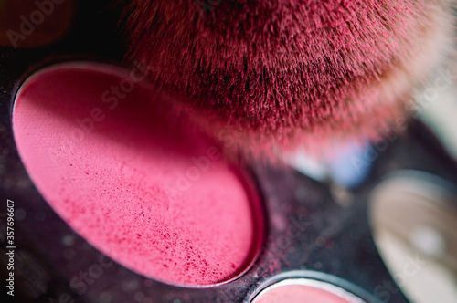 Frontal close up of a powder brush with pink particles on a blush pallet