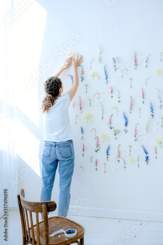 Girl decorates a wall with flowers. A lot of flowers of different colors fixed on a wall of white, blue, pink, yellow colors. Flower multicolored background.