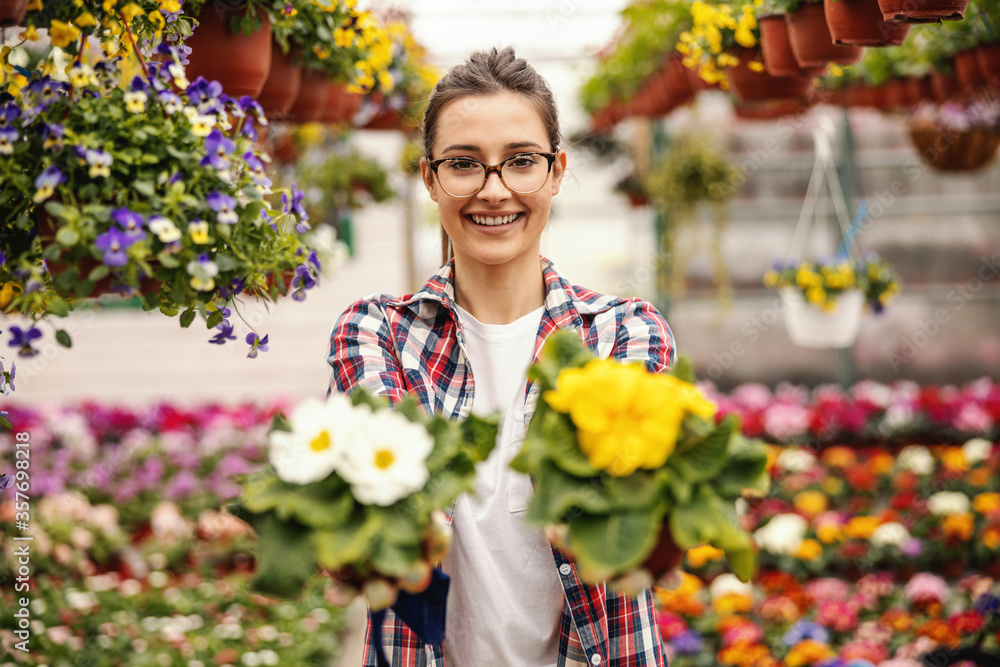 Young smiling female entrepreneur offering beautiful colorful flowers and looking at camera. Selective focus is on woman.