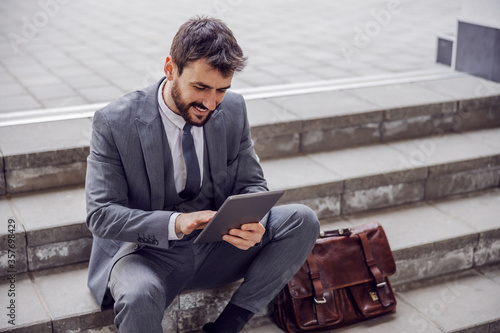Young businessman sitting on the stairs outdoors after work and using tablet.
