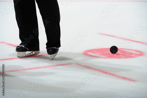 Ice hockey referee standing on ice. Closeup of referee trousers and skates. Face-off spot and a puck.