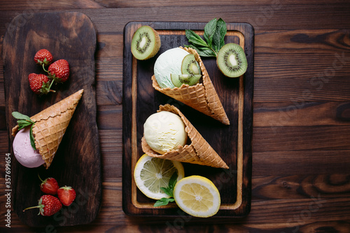 Various flavored ice cream scoops in waffle cones on wooden table. Food background, summer refreshment concept
