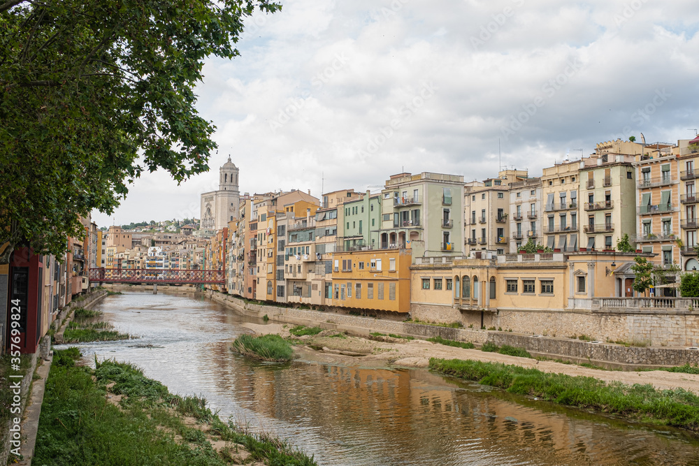 Fototapeta premium Girona's skyline on a cloudy day with water reflection river houses, bridge and massive cathedral on the horizon