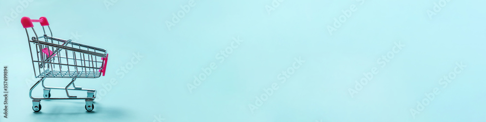 Simply minimal design with small supermarket grocery push cart for shopping toy with wheels isolated on blue pastel background. Sale buy mall market shop consumer concept. Copy space, banner Simply minimal design with small supermarket grocery push cart for shopping toy with wheels isolated on blue pastel background. Sale buy mall market shop consumer concept. Copy space, banner