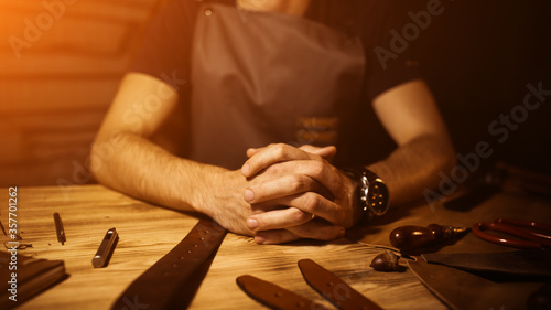Working process of the leather belt in the workshop.Man holding hands on wooden table.Crafting tools background. Tanner in old tannery.Interlock fingers.Warm Light for text and design.Web banner size