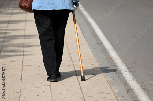 Woman walking with a cane on a street, female legs on pavement. Concept for disability, limping person, diseases of the spine, old people