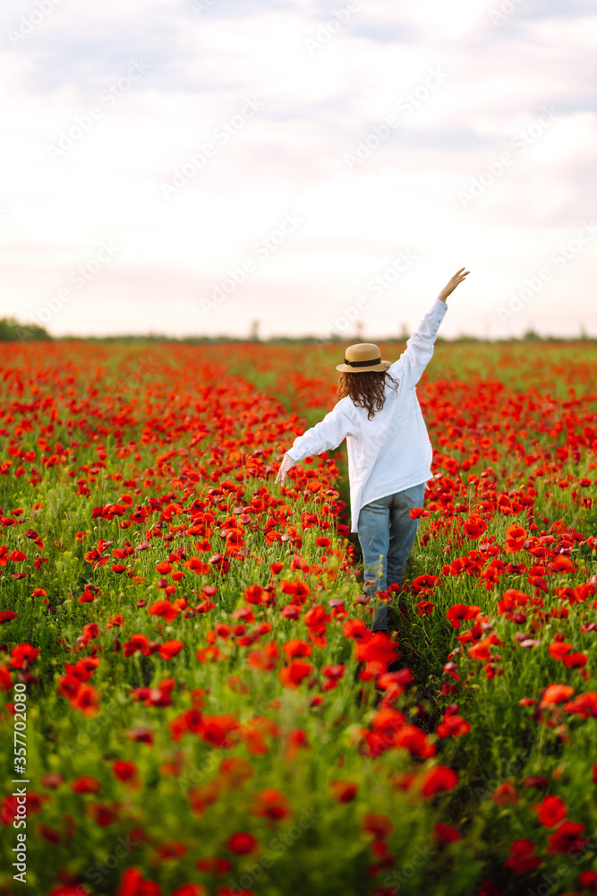 Young girl in hat posing in the poppy field. Portrait of curly girl walking in poppy field at sunset. Summertime. Young girl in hat posing in the poppy field. Portrait of curly girl walking in poppy field at sunset. Summertime.