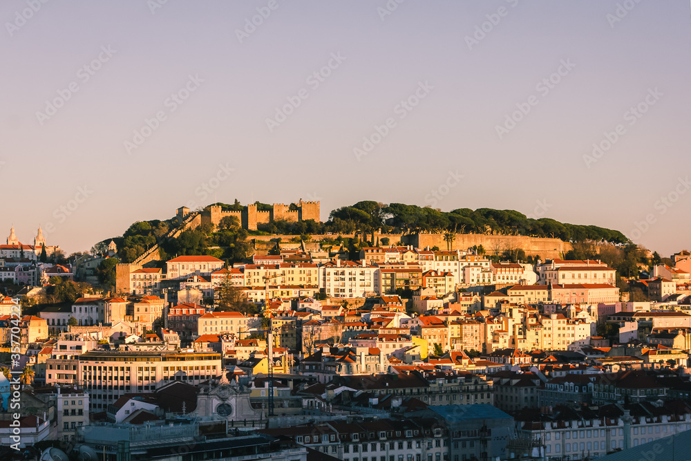 View of Sao Jorge Castle, Lisbon, Portugal, at sunset, with the downtown skyline in mid to foreground. Mediterranean travel concept