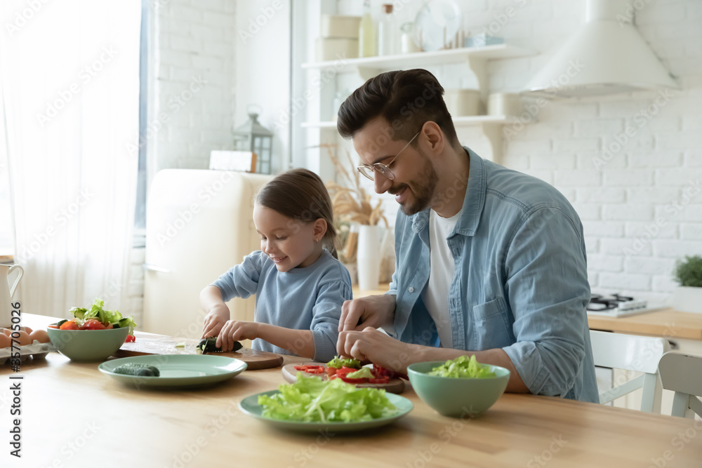 Father and small daughter cooking together, cutting vegetables fresh cucumber lettuce tomato and paprika for vegetarian salad. Healthy eating and lifestyle, teach develop kid, happy fatherhood concept Father and small daughter cooking together, cutting vegetables fresh cucumber lettuce tomato and paprika for vegetarian salad. Healthy eating and lifestyle, teach develop kid, happy fatherhood concept