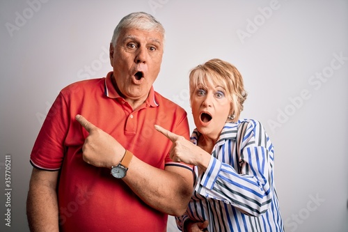 Senior beautiful couple standing together over isolated white background Surprised pointing with finger to the side, open mouth amazed expression.