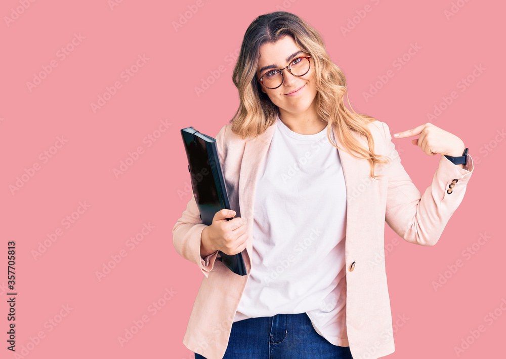 Naklejka premium Young caucasian woman wearing business clothes and glasses holding binder pointing finger to one self smiling happy and proud