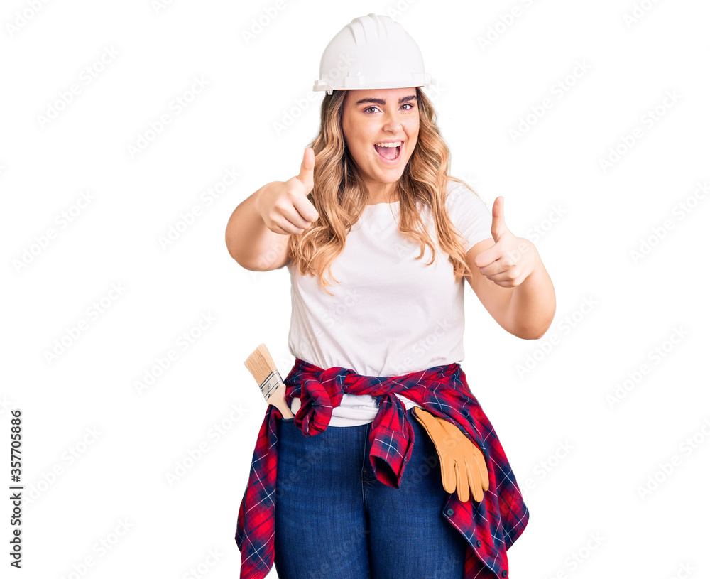 Young caucasian woman wearing security helmet approving doing positive gesture with hand, thumbs up smiling and happy for success. winner gesture. Young caucasian woman wearing security helmet approving doing positive gesture with hand, thumbs up smiling and happy for success. winner gesture.