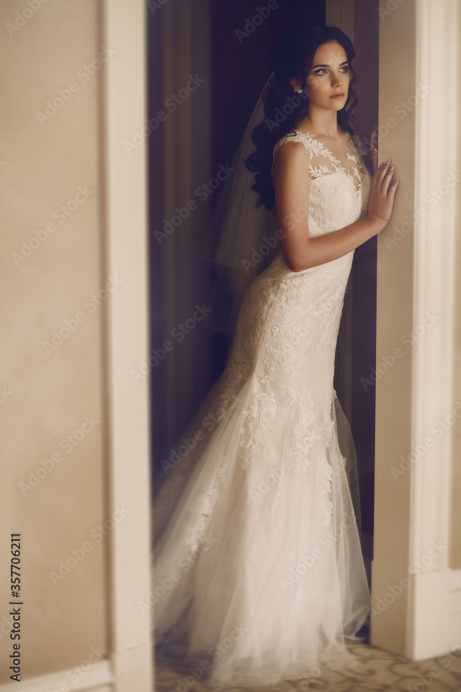 Fototapeta premium The morning of the bride. Beautiful girl in a white dress is preparing for the wedding ceremony. The beautiful young woman posing in a wedding dress. Fashion portrait of a beautiful bride