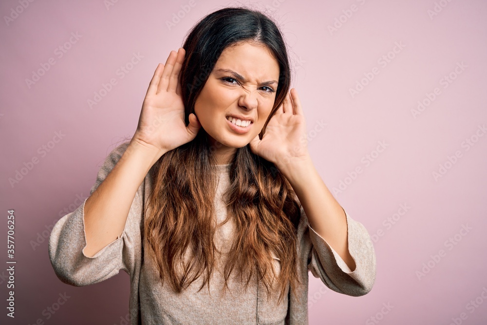 Young beautiful brunette woman wearing casual sweater standing over pink background Trying to hear both hands on ear gesture, curious for gossip. Hearing problem, deaf Young beautiful brunette woman wearing casual sweater standing over pink background Trying to hear both hands on ear gesture, curious for gossip. Hearing problem, deaf