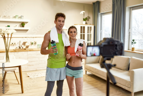 Physical Education. Young couple in sportswear recording video blog or vlog about healthy lifestyle on camera after exercising at home. Fitness, workout and vlogging concept
