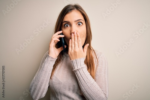 Young woman having a conversation speaking on smartphone over isolated background cover mouth with hand shocked with shame for mistake, expression of fear, scared in silence, secret concept