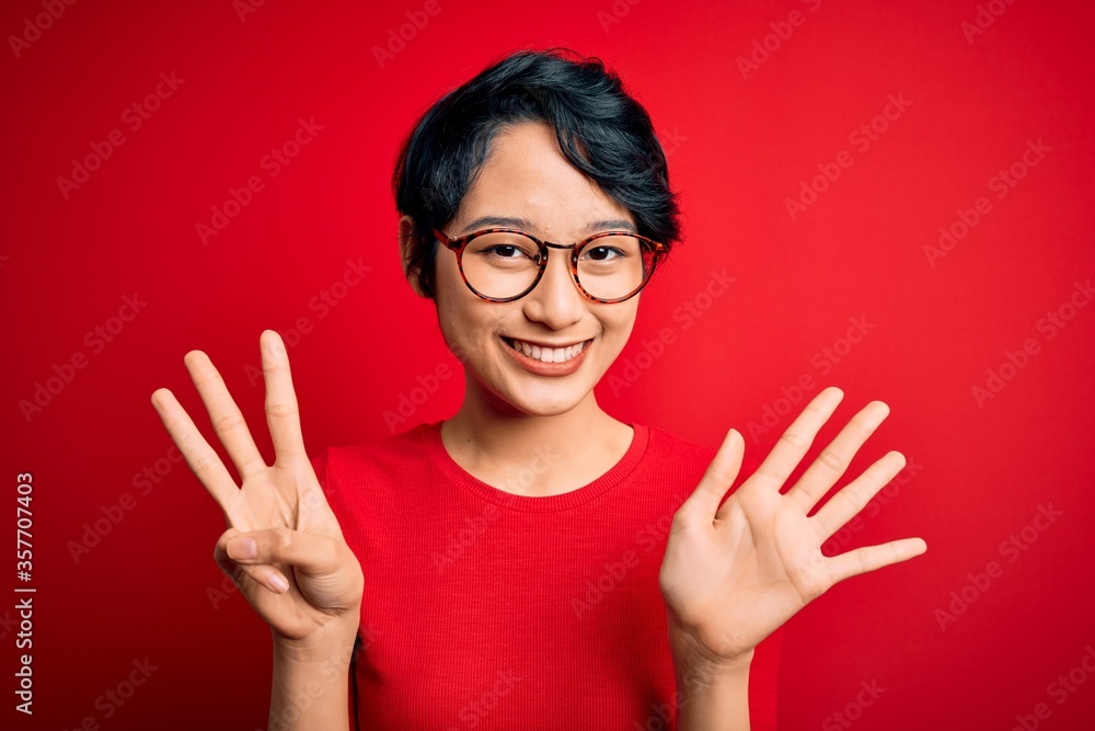 Young beautiful asian girl wearing casual t-shirt and glasses over isolated red background showing and pointing up with fingers number eight while smiling confident and happy. Young beautiful asian girl wearing casual t-shirt and glasses over isolated red background showing and pointing up with fingers number eight while smiling confident and happy.