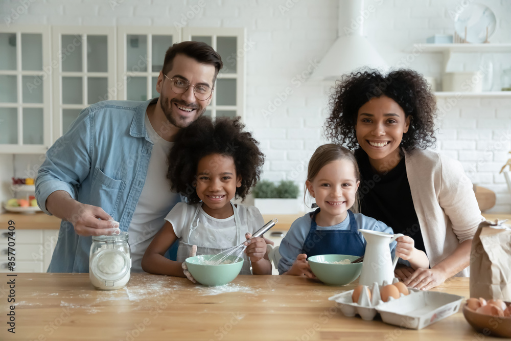 Multiethnic family with kids engaged in holiday cake preparation using fresh products mixing eggs milk flour ingredient looking at camera. Teach children, happy parenthood, common hobby, unity concept Multiethnic family with kids engaged in holiday cake preparation using fresh products mixing eggs milk flour ingredient looking at camera. Teach children, happy parenthood, common hobby, unity concept